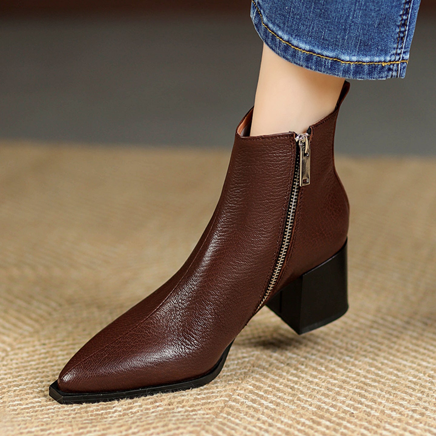 Brown leather ankle boot with a zipper on a textured surface