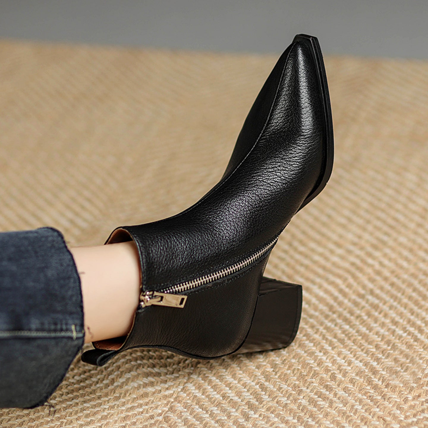 Black leather ankle boot with a gold zipper on a textured surface