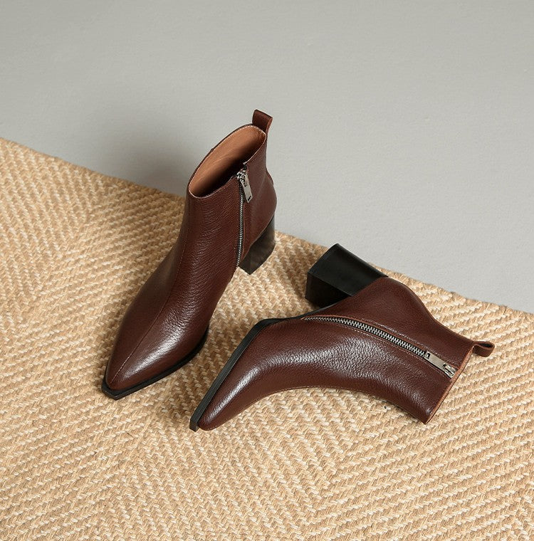 Pair of brown leather ankle boots with zippers on a textured surface.