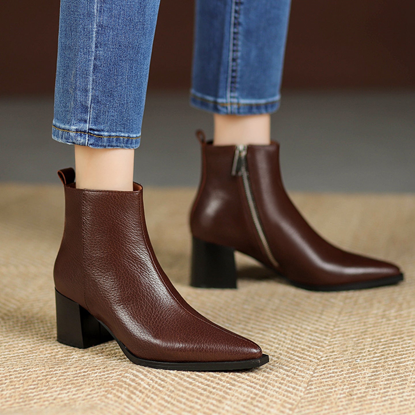 Brown ankle boots worn with blue jeans on a textured surface