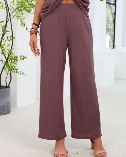Person wearing mauve pants standing in a bright room with a plant in the background