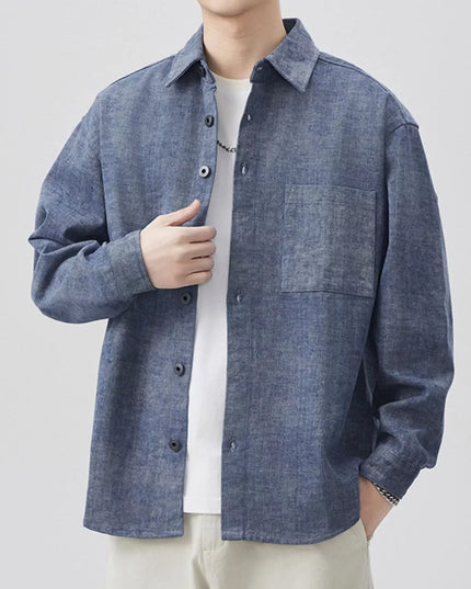 Person wearing a blue denim shirt over a white shirt on a light gray background