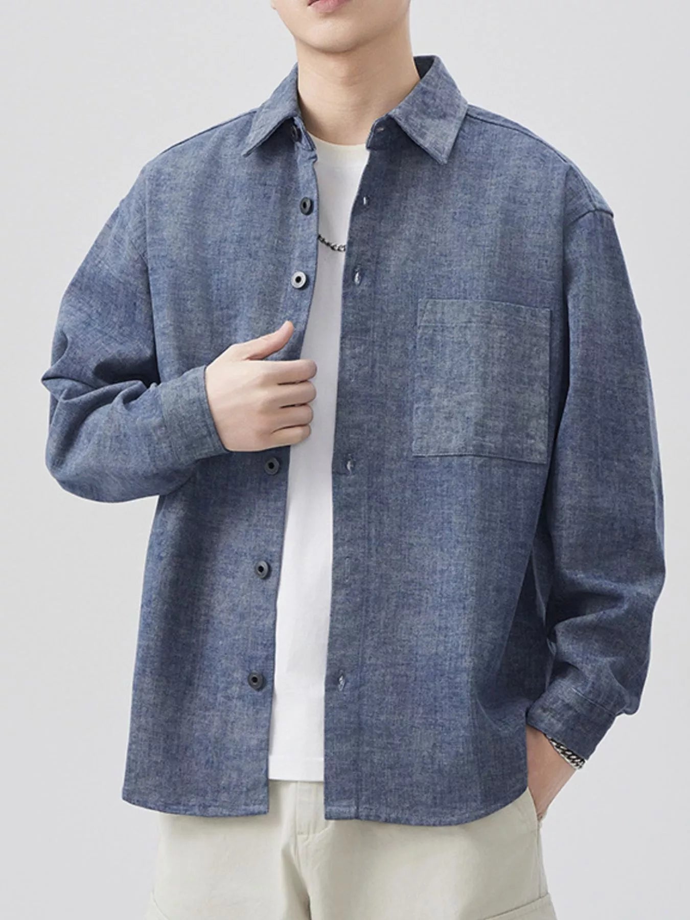 Person wearing a blue denim shirt over a white shirt on a light gray background