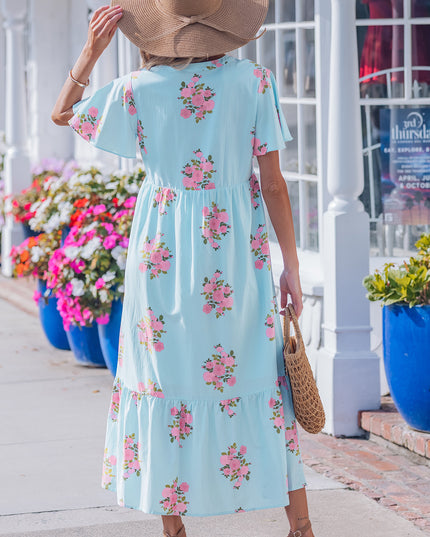 Woman in a floral dress walking on a sidewalk with flowers and a store in the background