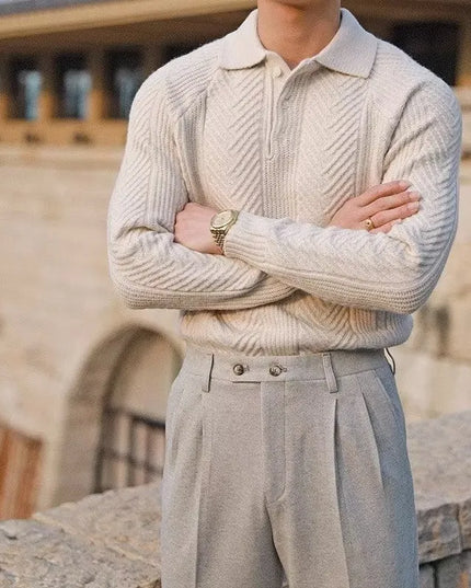 Person wearing a beige knitted sweater and light gray pants standing outdoors.