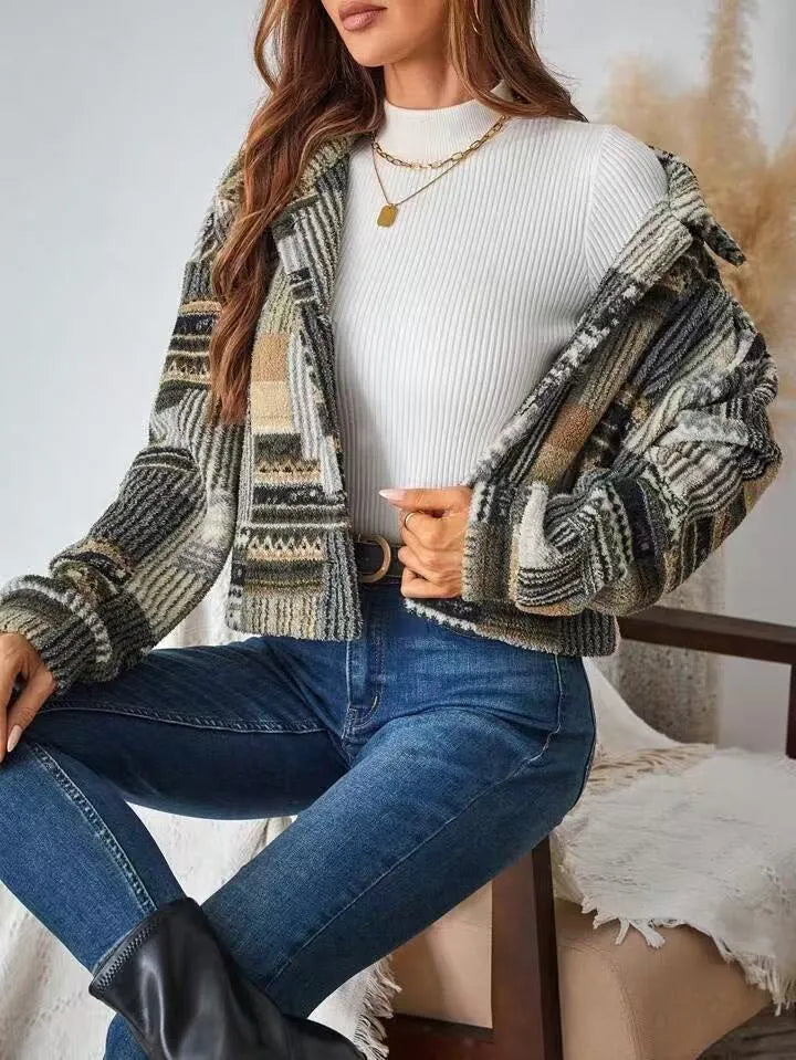 Woman wearing a patterned jacket, white sweater, and blue jeans sitting on a chair.