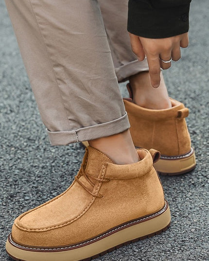 Tan suede boots worn with beige pants on a gray pavement background