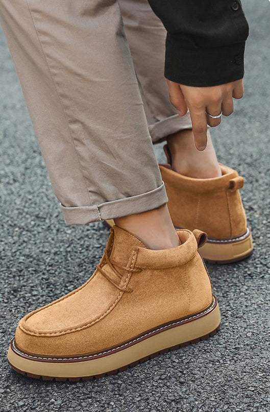 Tan suede boots worn with beige pants on a gray pavement background
