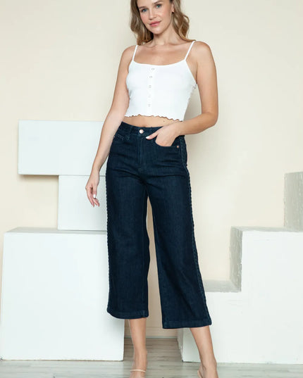 Woman wearing a white top and dark blue jeans standing against a light background