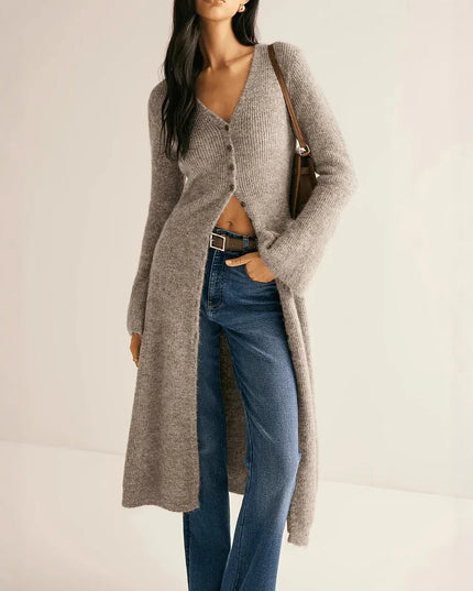 Woman wearing a long beige cardigan and blue jeans on a plain background