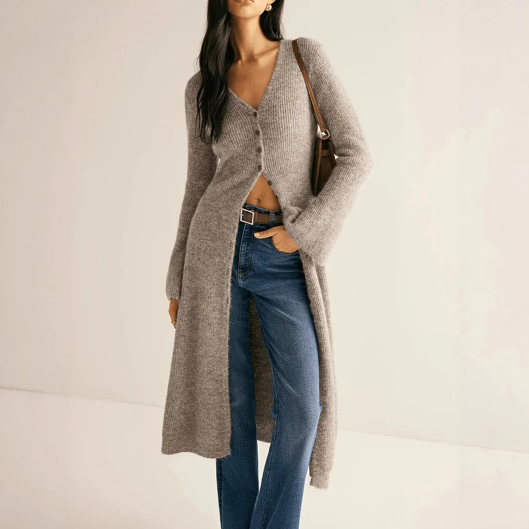 Woman wearing a long beige cardigan and blue jeans on a plain background
