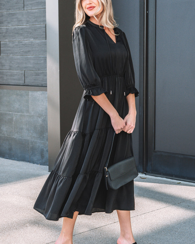 Woman wearing a black dress with a black clutch against a gray wall.