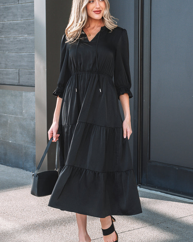 Woman wearing a black dress standing against a gray wall.