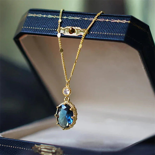 Gold necklace with a blue pendant on a dark surface