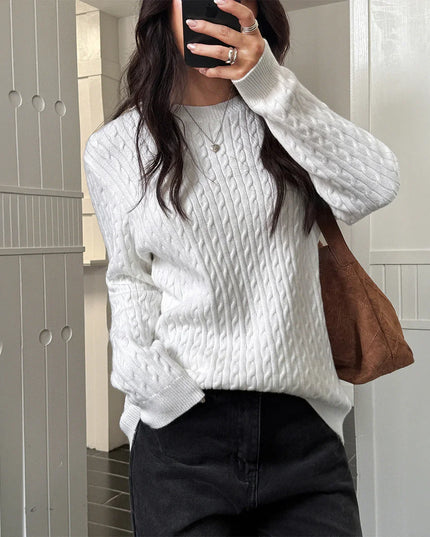 Person wearing a white cable knit sweater and holding a brown bag.