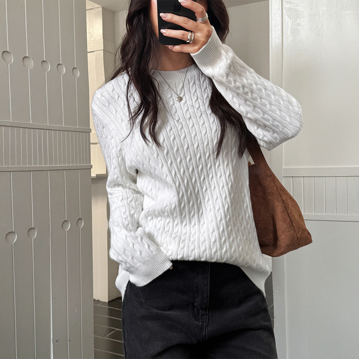 Person wearing a white cable knit sweater and holding a brown bag.