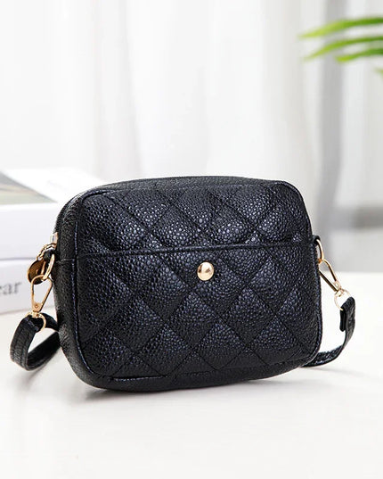 Black quilted handbag on a white surface with a blurred background