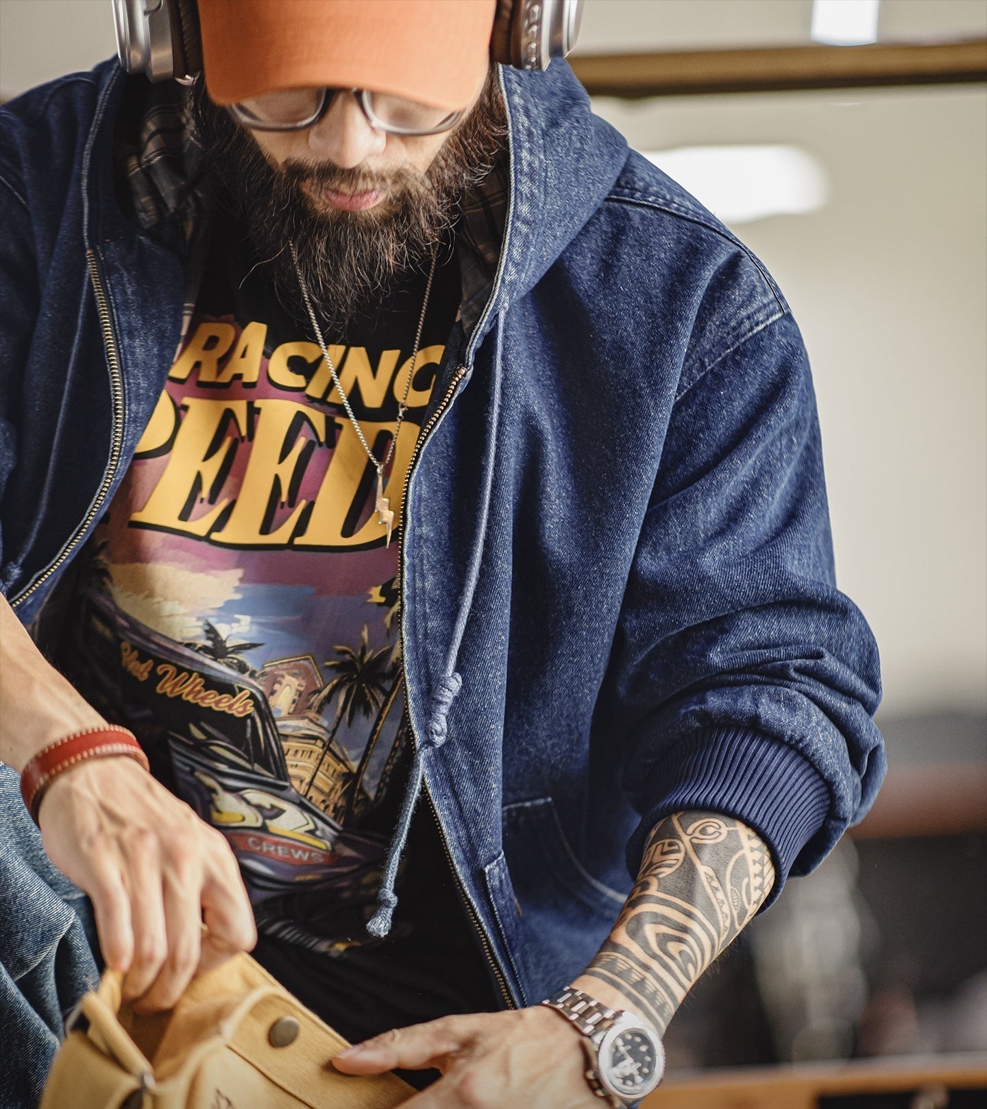 Man wearing a denim jacket and 'Racing Speed' t-shirt, holding a leather bag.