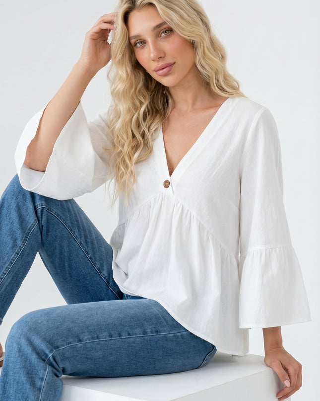 Woman wearing a white blouse and blue jeans sitting on a white block against a white background