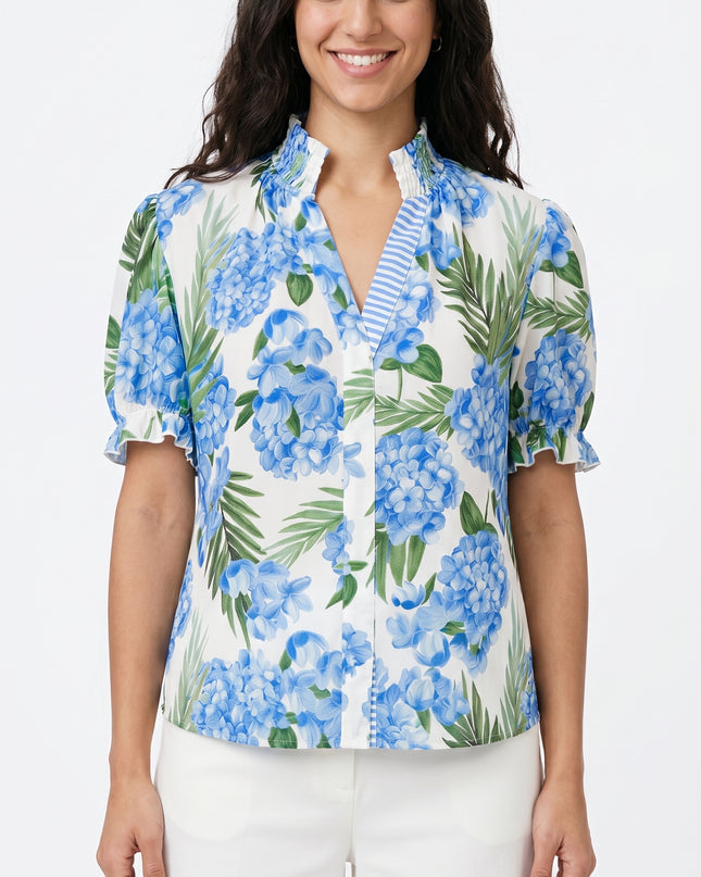 Woman wearing a blue floral blouse with white pants on a white background