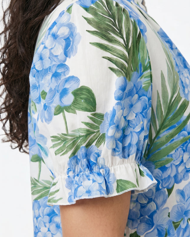 Close-up of a person wearing a floral blouse with blue flowers and green leaves.