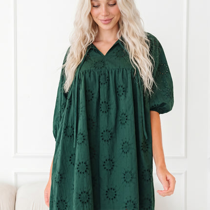 Woman wearing a green dress with puff sleeves against a white wall.
