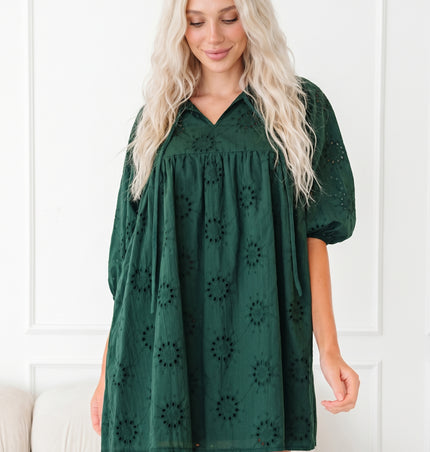 Woman wearing a green dress with puff sleeves against a white wall.