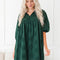 Woman wearing a green dress with puff sleeves against a white wall.