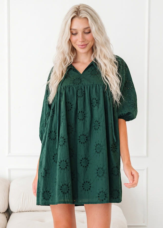 Woman wearing a green dress with puff sleeves against a white wall.