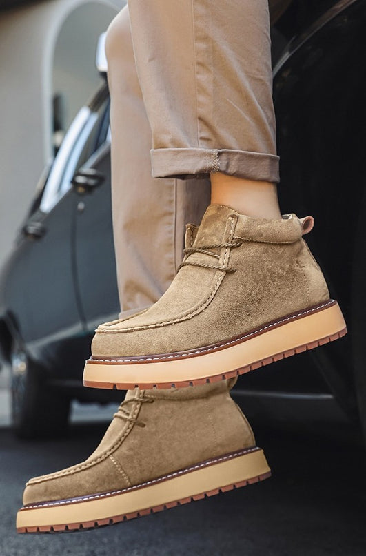 Brown suede boots with beige soles worn by a person, with a car in the background.