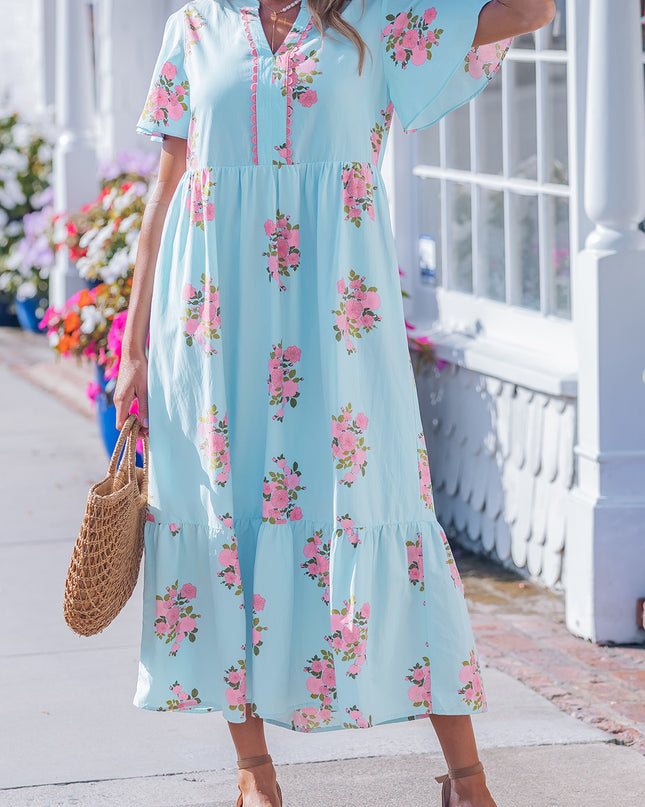 Woman wearing a light blue floral dress standing on a porch.