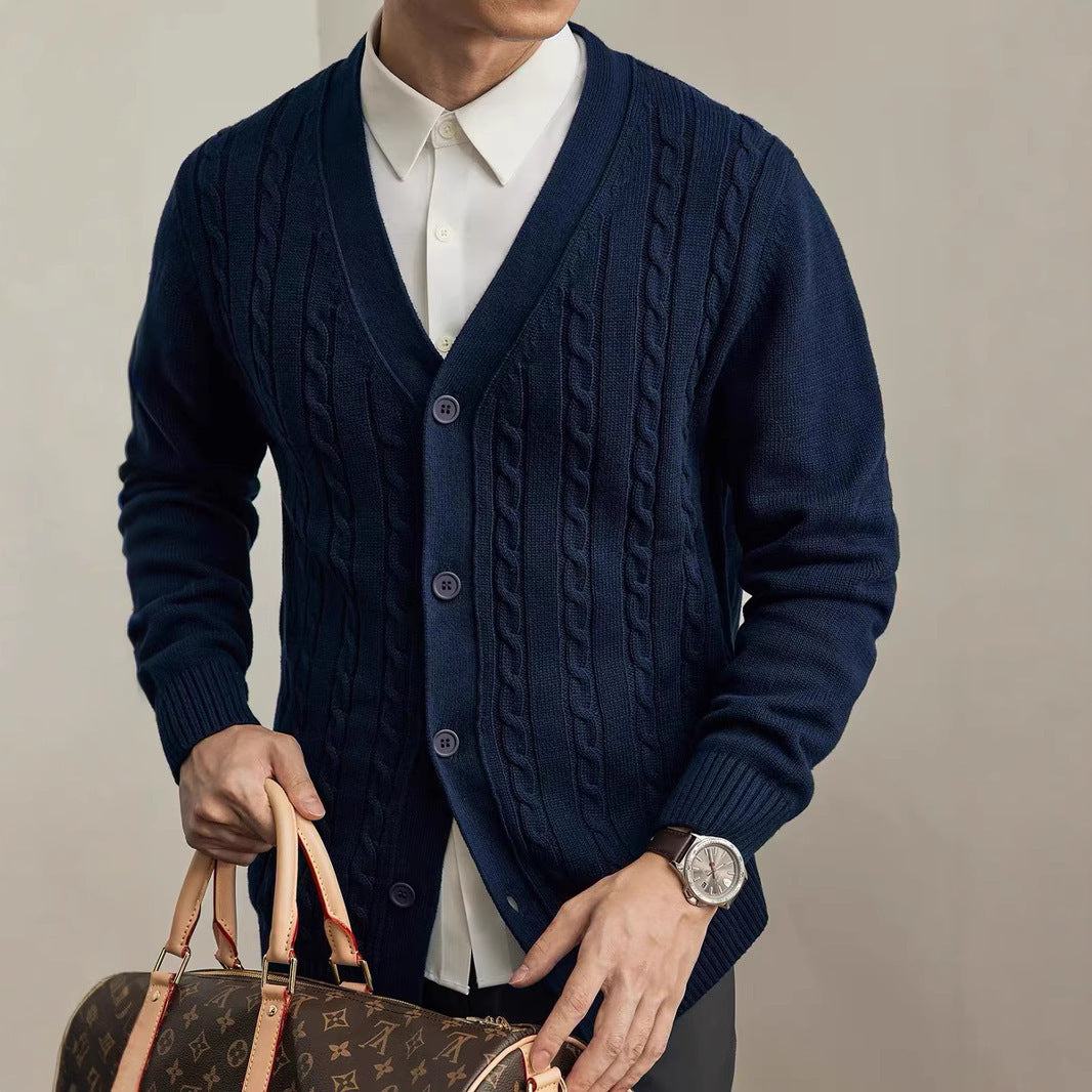 Person wearing a navy blue cable knit cardigan holding a brown leather handbag against a neutral background