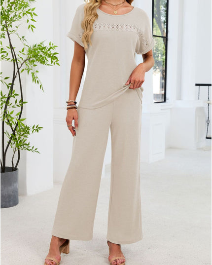 Woman wearing a beige jumpsuit standing in a bright room with a plant.