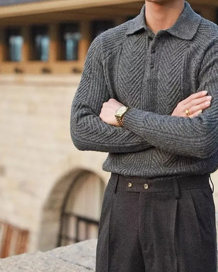 Person wearing a gray knitted sweater and dark pants with a blurred architectural background