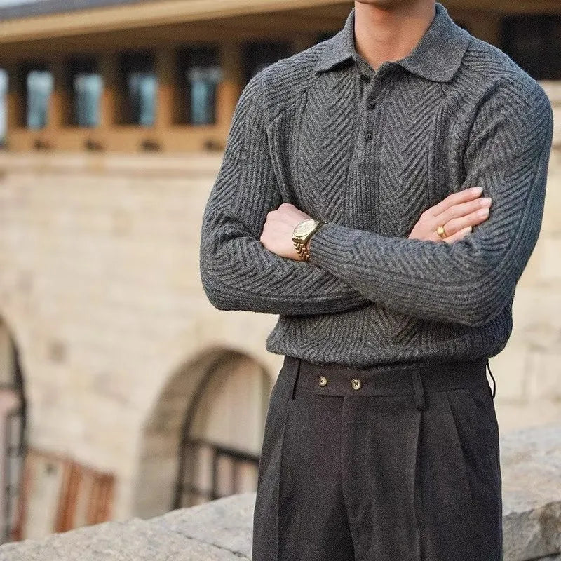 Person wearing a gray knitted sweater and dark pants with a blurred architectural background