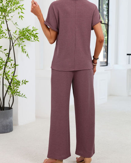 Person wearing a mauve outfit standing in a bright room with a plant.