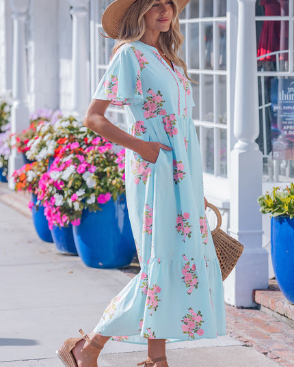Woman in a light blue floral dress walking outdoors with flowers and a building in the background