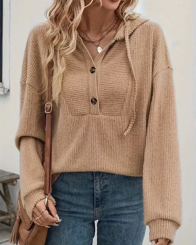 Person wearing a beige ribbed sweater with a hood, holding a brown bag indoors.