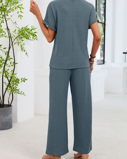 Person wearing a blue outfit standing in a bright room with a plant.