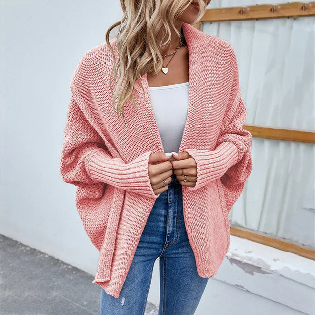 Woman wearing a pink knitted cardigan over a white top and blue jeans.
