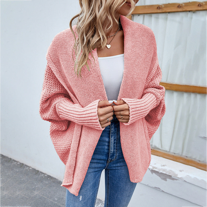 Woman wearing a pink knitted cardigan over a white top and blue jeans.