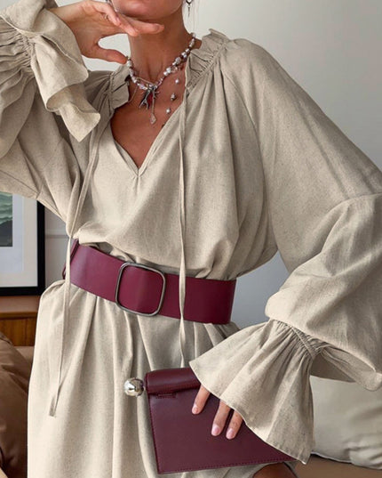 Woman wearing a beige dress with a maroon belt and clutch, indoors.