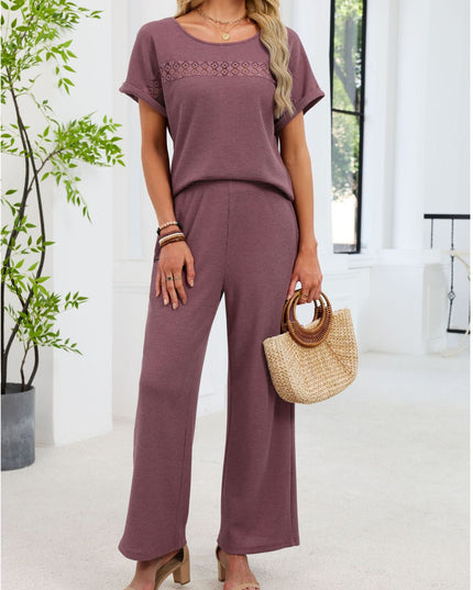 Woman wearing a purple outfit with wide-leg pants, holding a straw bag indoors.
