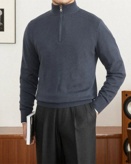 Person wearing a blue half-zip sweater and dark pants in a room with wooden furniture and a framed picture.
