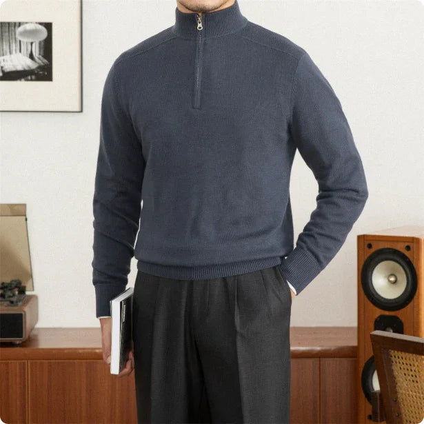 Person wearing a blue half-zip sweater and dark pants in a room with wooden furniture and a framed picture.