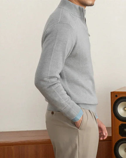 Person wearing a gray sweater and beige pants standing next to a wooden speaker.