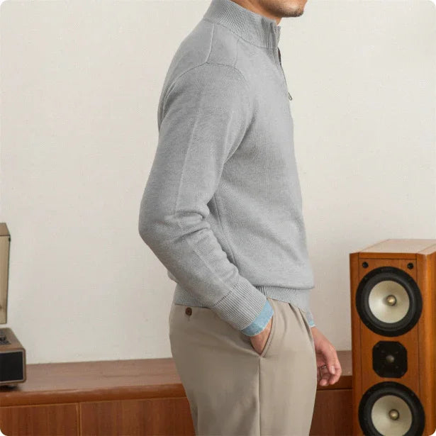 Person wearing a gray sweater and beige pants standing next to a wooden speaker.
