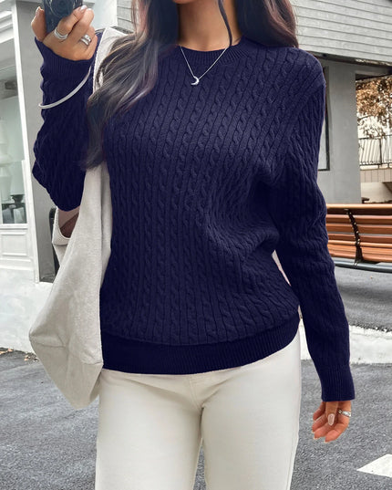 Person wearing a navy blue cable knit sweater and white pants, standing outdoors.