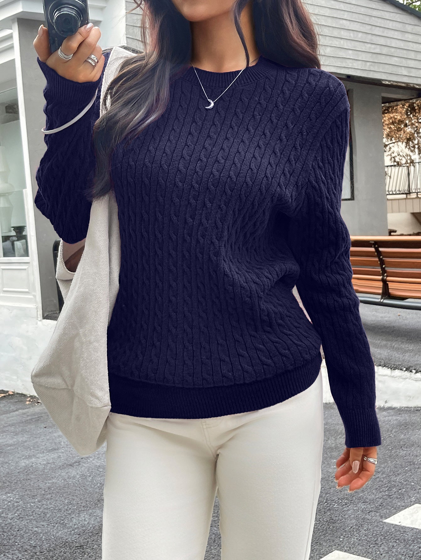 Person wearing a navy blue cable knit sweater and white pants, standing outdoors.