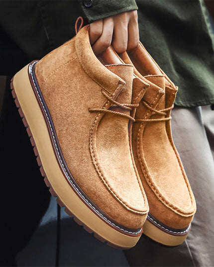 Brown suede shoes held by a person wearing a green jacket and beige pants.